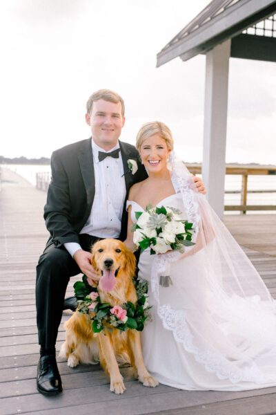 Bride and groom posing with a golden retriever on their wedding day.