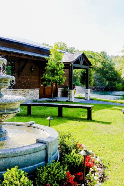 Elegant stone fountain in a sunny garden with greenery and flowers.