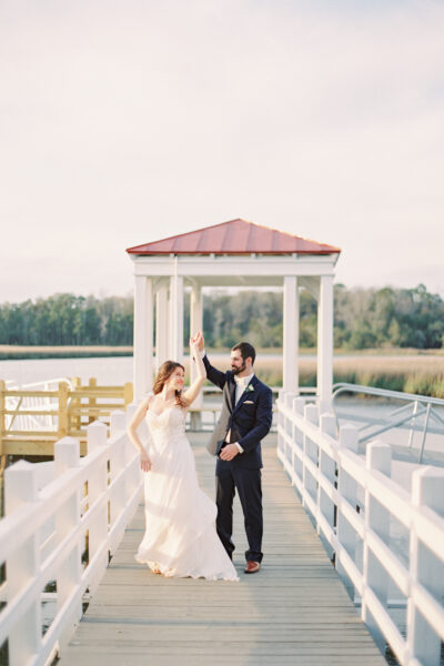 Bride and groom dancing on a pier by the water.