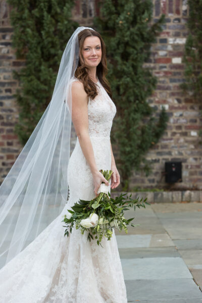 Bride in a lace wedding dress holding a bouquet with a long veil.