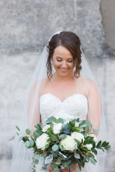 Bride in a strapless lace wedding dress holding a bouquet and smiling.