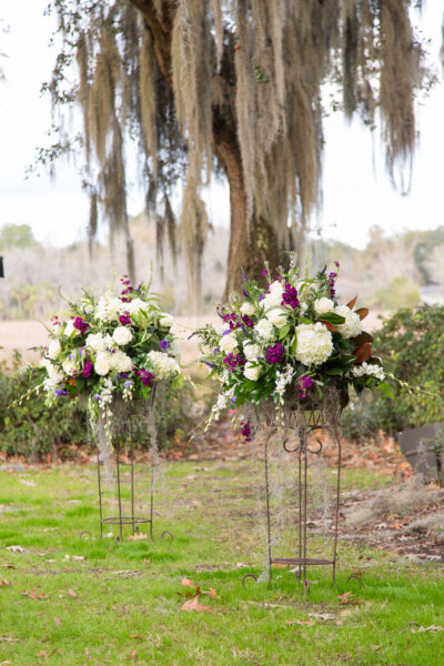 Elegant white and purple floral arrangements on stands outdoors.