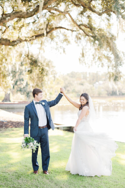 Bride and groom dancing outdoors by a lake during sunset.