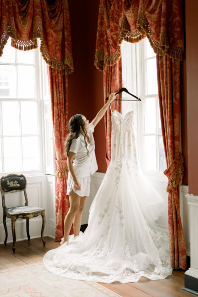 Bride lifting her wedding dress in a sunlit room.