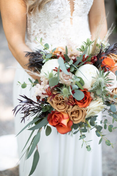A vibrant bridal bouquet with orange, white, and tan flowers accented by greenery.
