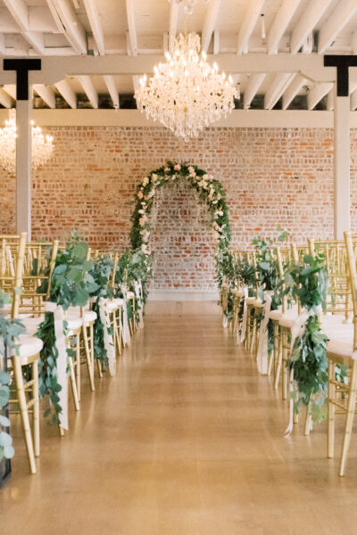 Elegant indoor wedding aisle with floral decorations and a chandelier.