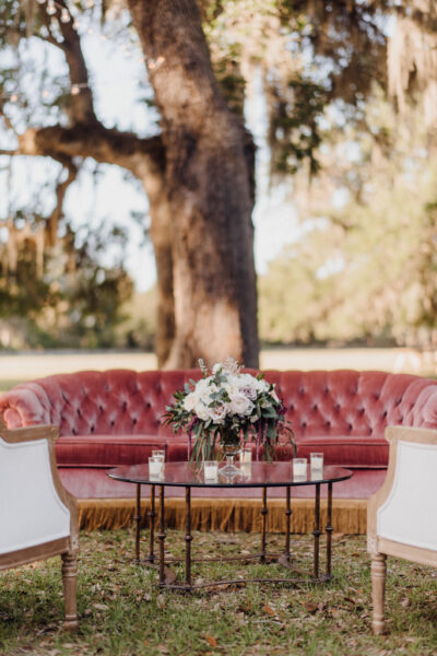 Elegant floral arrangement on a table between plush red and white seating outdoors.