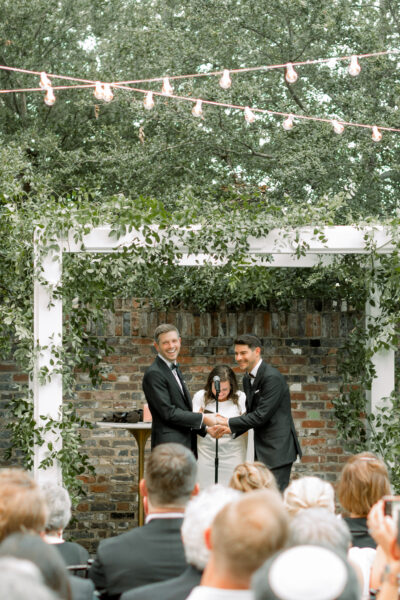 Couple exchanges vows under floral arch during outdoor wedding ceremony.