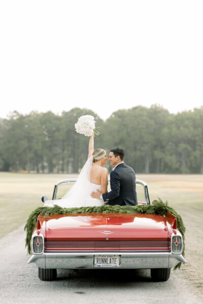 Newlyweds share a kiss in a decorated red convertible after their wedding.