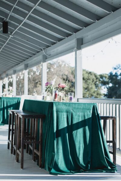 Outdoor dining area with green tablecloths and bar stools on a porch.