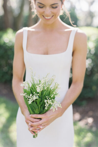 Bride in white dress holding a bouquet of lily of the valley flowers.