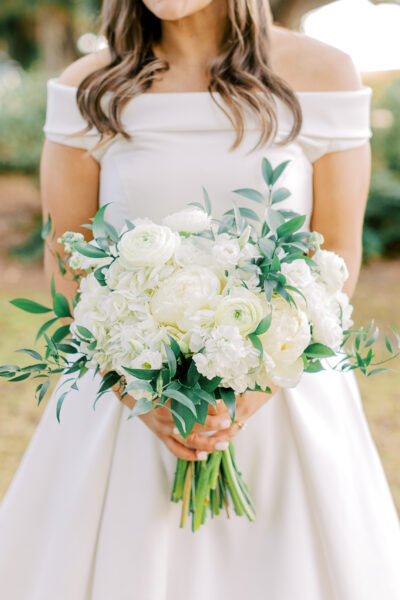 Bride holding a lush white floral bouquet with greenery.