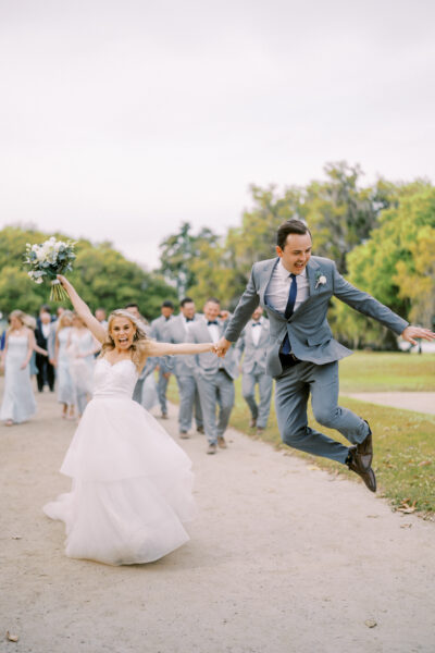 Bride and groom joyfully celebrating outdoors with wedding party in the background.