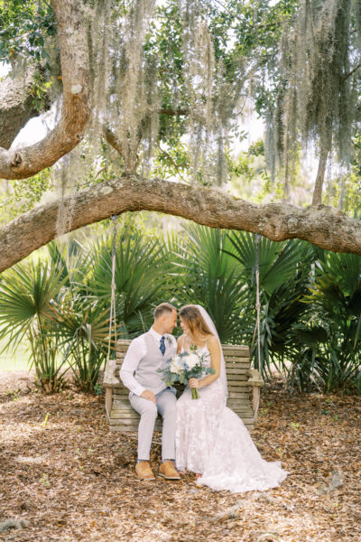 Bride and groom share a tender kiss under a large tree in a lush garden.