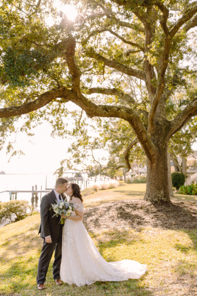 Bride and groom share a kiss under a large tree on their wedding day.
