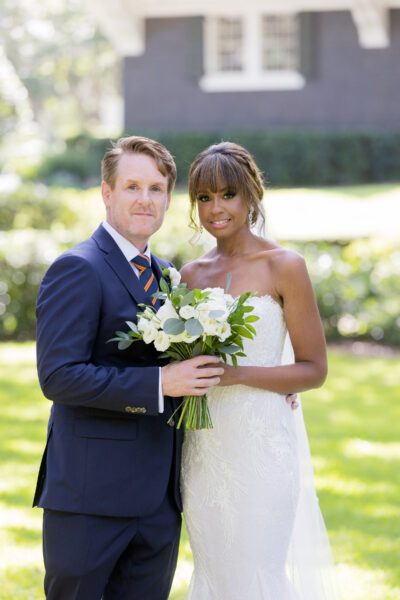 Bride and groom posing outdoors with a bouquet on their wedding day.