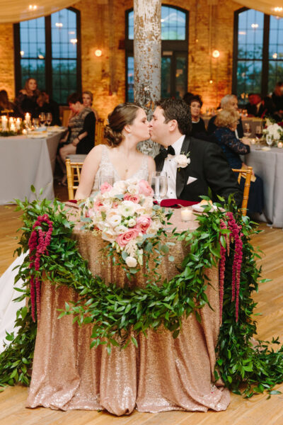 Bride and groom share a kiss at their beautifully decorated sweetheart table.