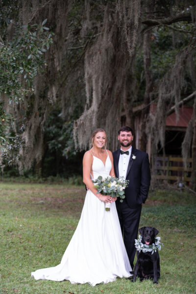 Bride and groom posing outdoors under a large tree on their wedding day.