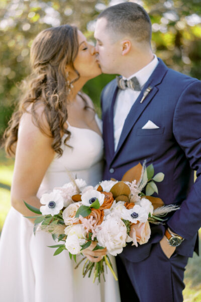 A bride and groom sharing a kiss, bride holding a beautiful bouquet.
