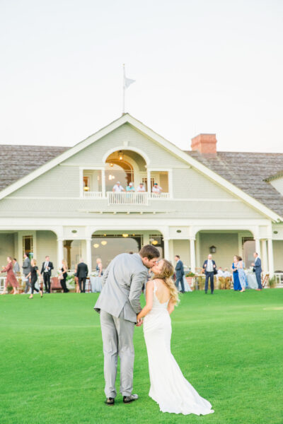Bride and groom share a kiss in front of a classic white house during their wedding.