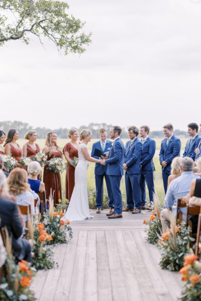 Bride and groom exchanging vows outdoors with bridesmaids and groomsmen.