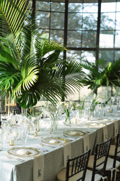 Elegant table setting with glassware and tropical palm leaves in a bright room.