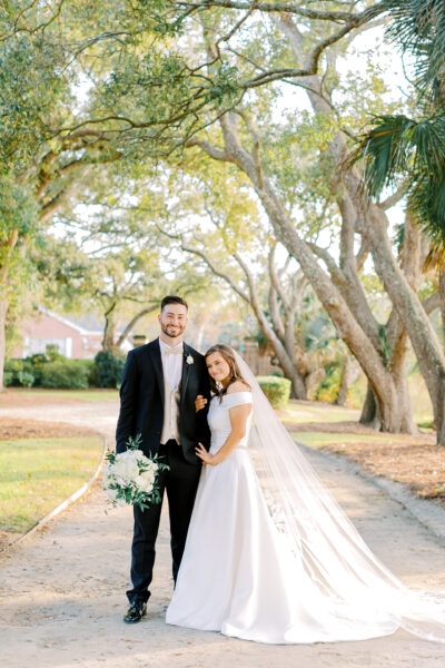 Newlywed couple posing happily outdoors under sunlit trees.