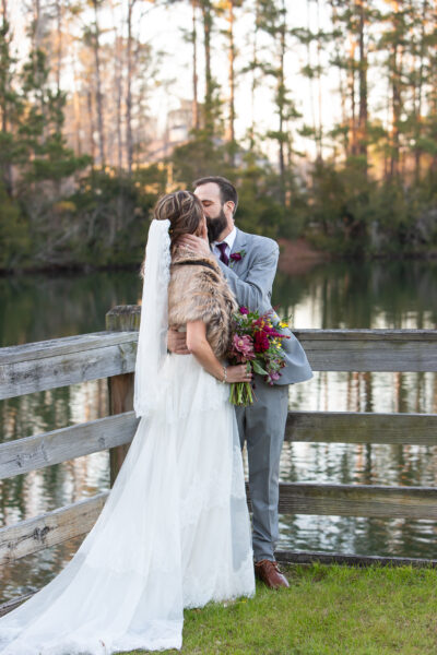 Bride and groom sharing a kiss on a wooden dock at sunset.