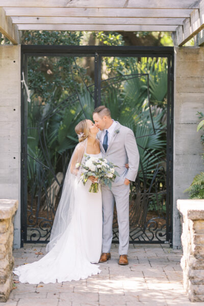 Bride and groom share a kiss in a lush garden setting.