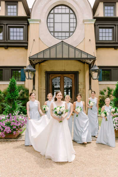 Bride with bridesmaids holding bouquets outside a charming building.