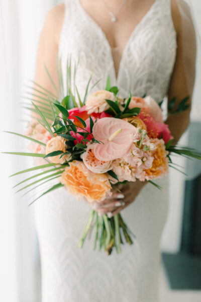 Bride holding a vibrant bouquet of pink, orange, and red flowers with greenery.