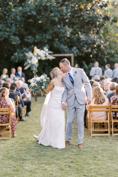 Newlywed couple kisses joyfully during outdoor wedding ceremony.