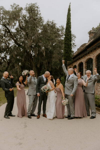 A joyful wedding party celebrating outdoors in elegant attire.