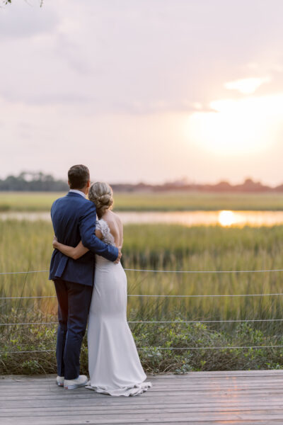 A couple embraces while watching the sunset over a serene field.
