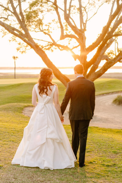 Bride and groom holding hands at sunset on a golf course.
