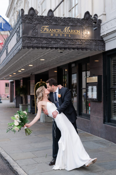 Bride and groom share a romantic dip kiss outside a theater.
