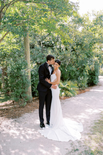 A couple embraces in a sunlit garden on their wedding day.