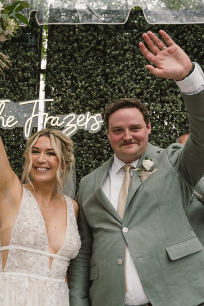 Newlywed couple joyfully waving, celebrating their wedding day.