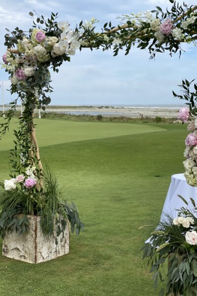 Floral arch set up on a grassy field with a clear sky and distant water view.