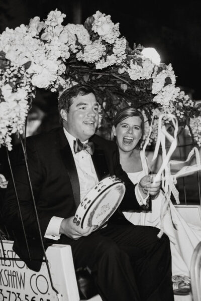 A joyful couple dressed formally, sitting under a floral arch at night.