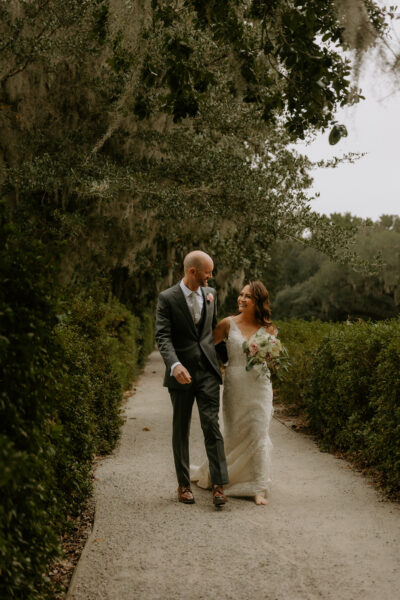 A couple walks hand-in-hand down a tree-lined path on their wedding day.