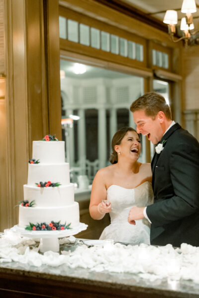 Bride and groom laughing while cutting their wedding cake.