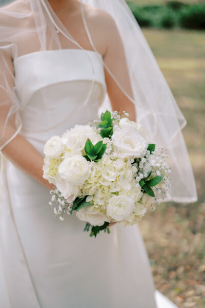 Bride holding a bouquet of white flowers and greenery.