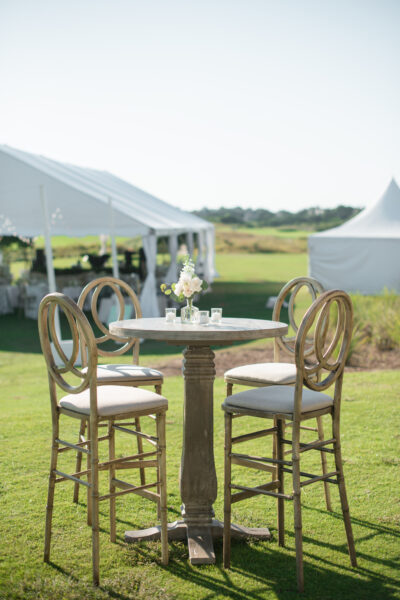 Elegant outdoor dining setup with wooden chairs and a round table under white tents.