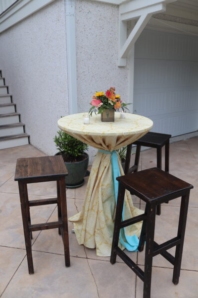 A small outdoor table with floral centerpiece and three wooden stools.