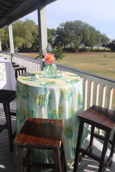 Outdoor table with a floral tablecloth and centerpiece on a porch.