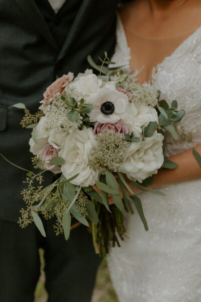 A bride holding a white and pink floral bouquet with greenery.