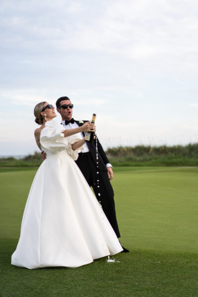 Bride and groom celebrating with champagne on a golf course.