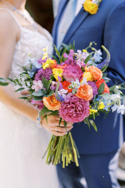 Bride and groom holding a vibrant wedding bouquet with colorful flowers.