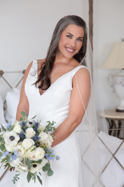 Bride in a white wedding dress holding a bouquet of white and blue flowers.